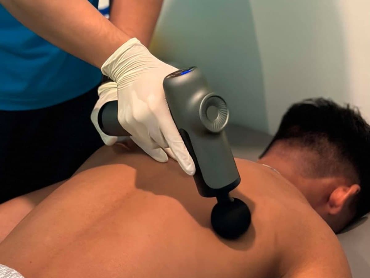 Therapist using a massage gun on a patient's shoulder