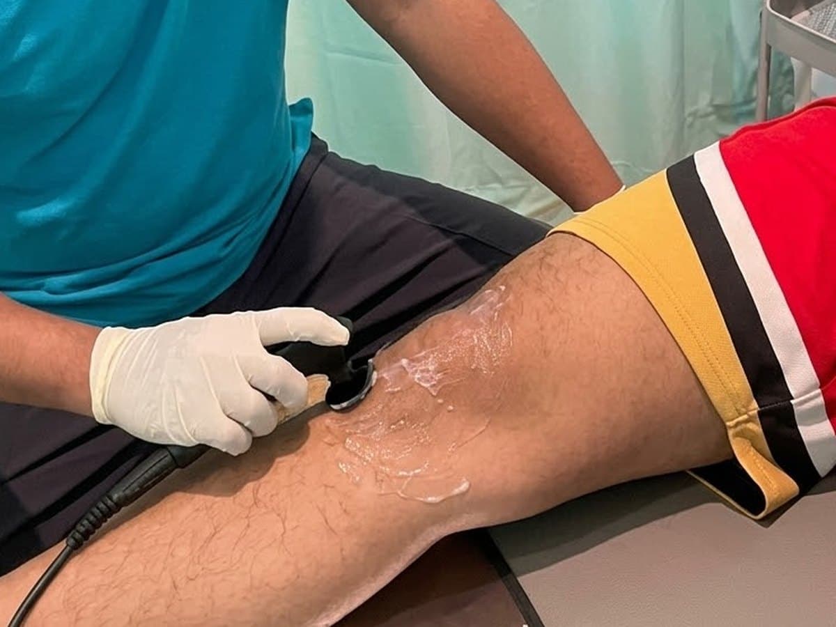 Therapist gliding a Tecar handpiece over gel on a patient's knee