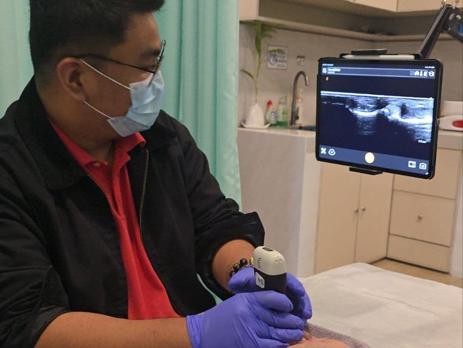 Doctor scanning a patient's hand with a handheld ultrasound probe beside the live scan on a tablet
